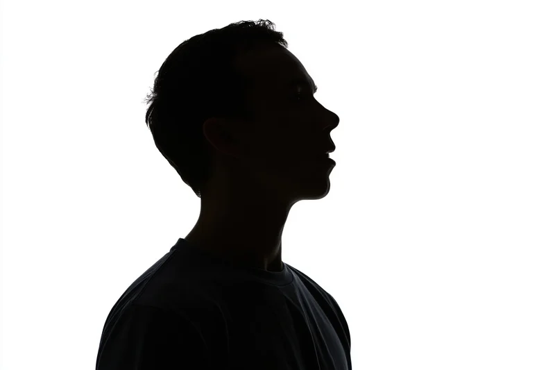 Silhouette of a young man in profile looking upward against white background