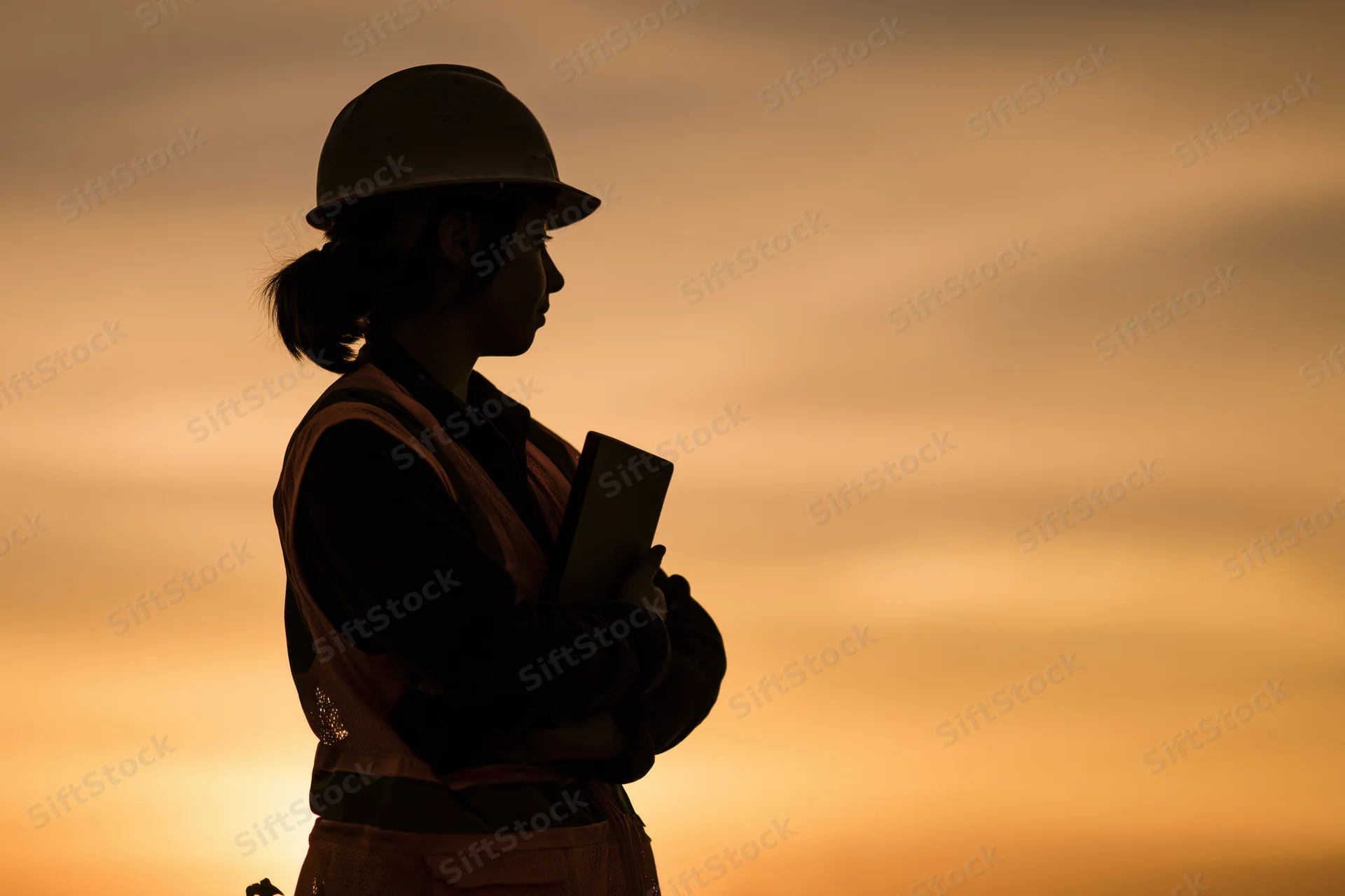 Silhouette of a female construction engineer holding a tablet outdoors at sunset