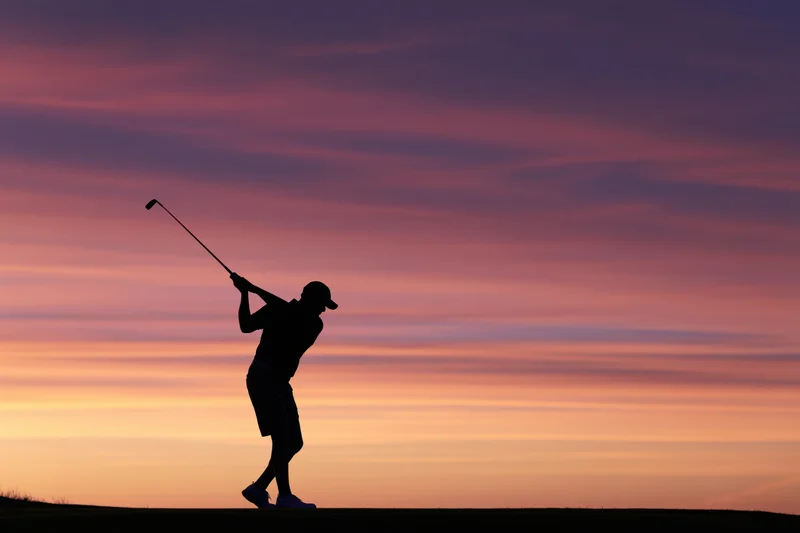 Silhouette of a golfer completing a full follow-through swing at sunset