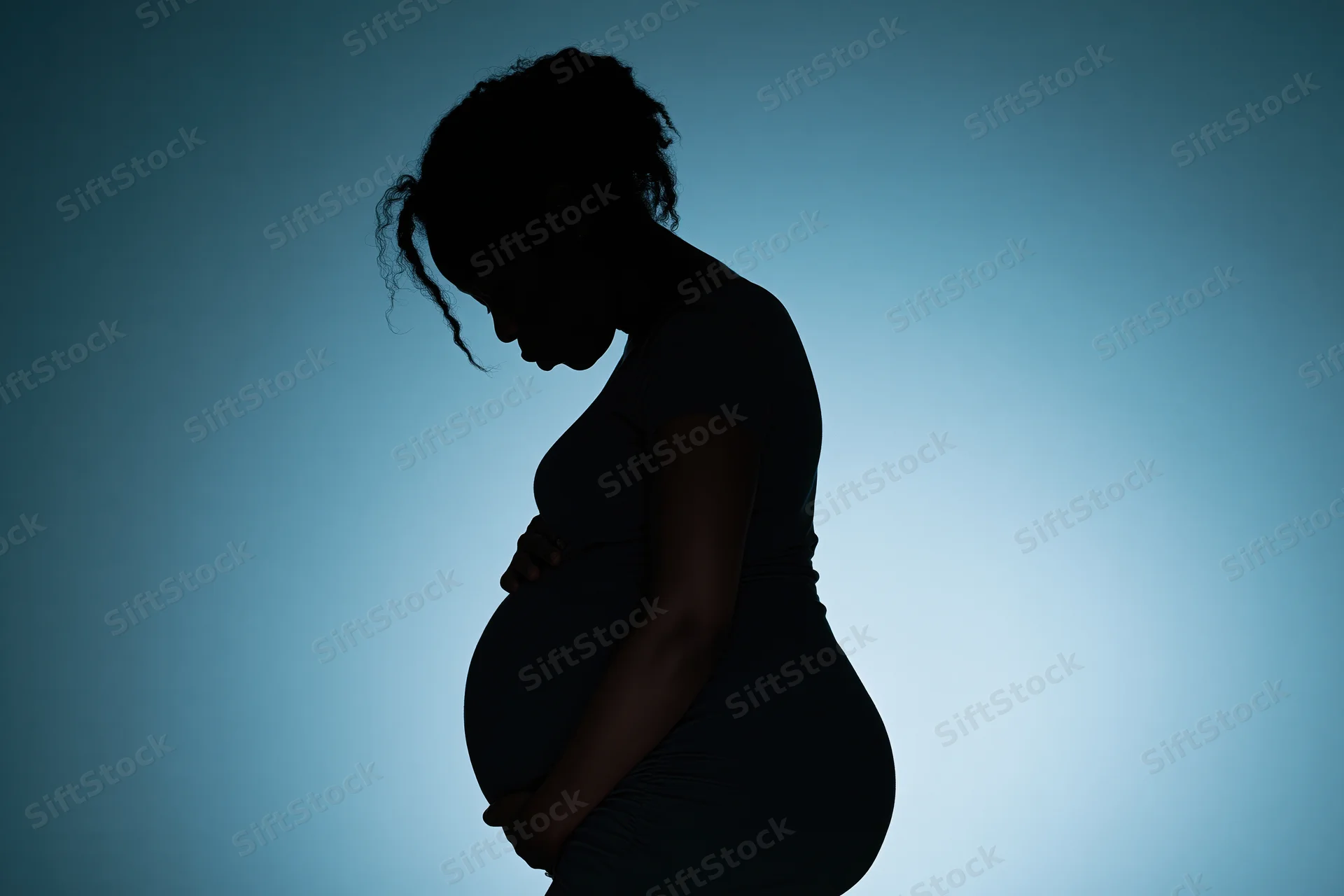 Silhouette of pregnant woman in profile holding her belly against blue gradient background