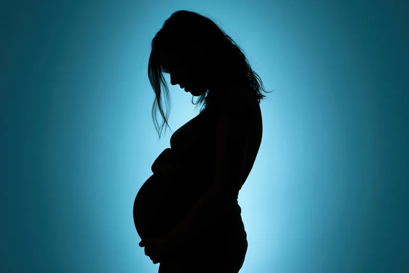 Silhouette of pregnant woman in profile holding her belly against blue background