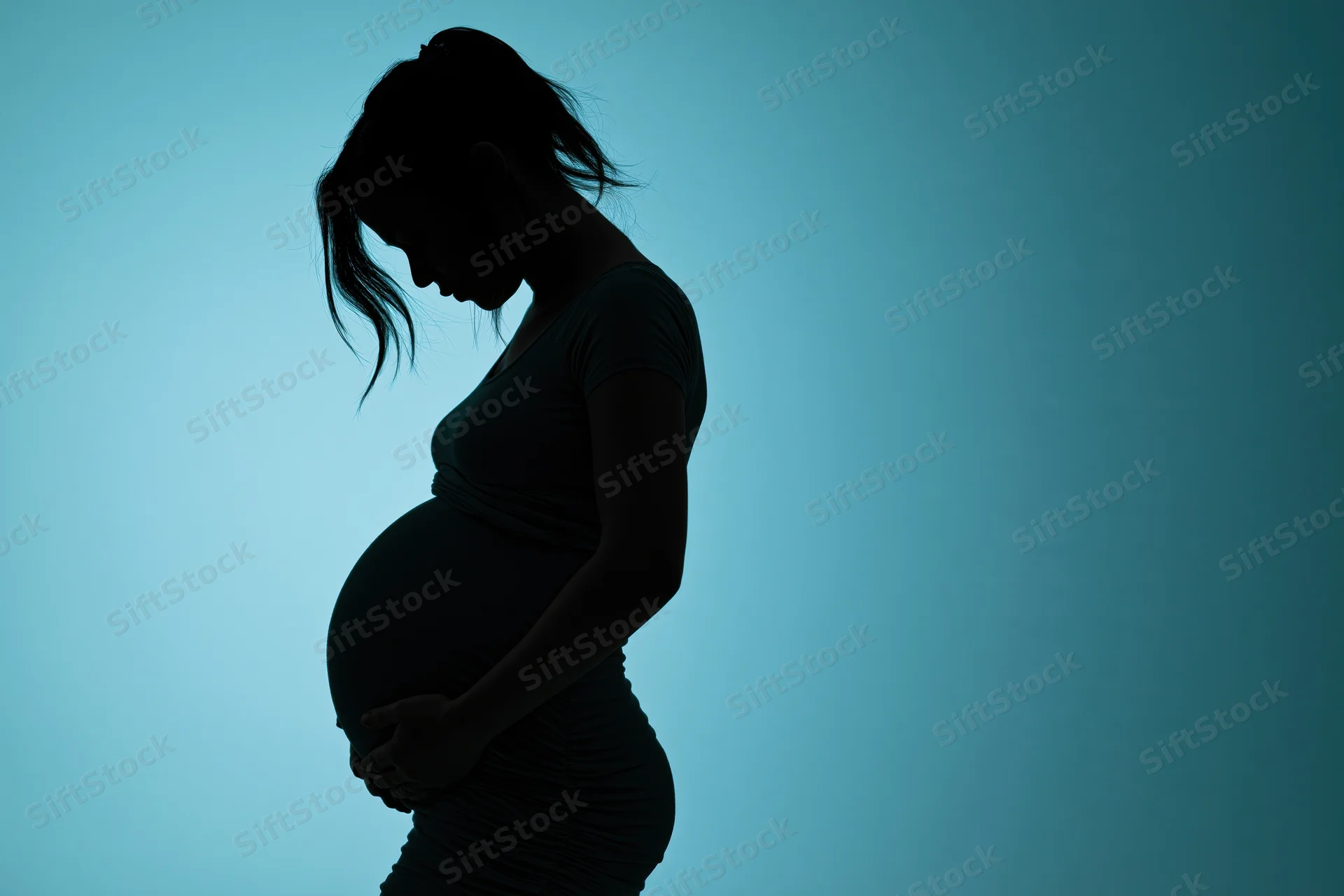 Silhouette of pregnant woman in profile holding her belly against blue background