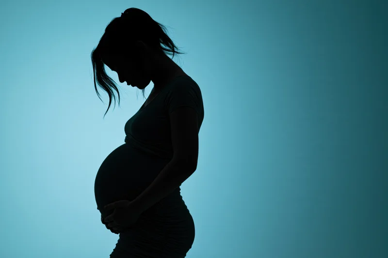 Silhouette of pregnant woman in profile holding her belly against blue background