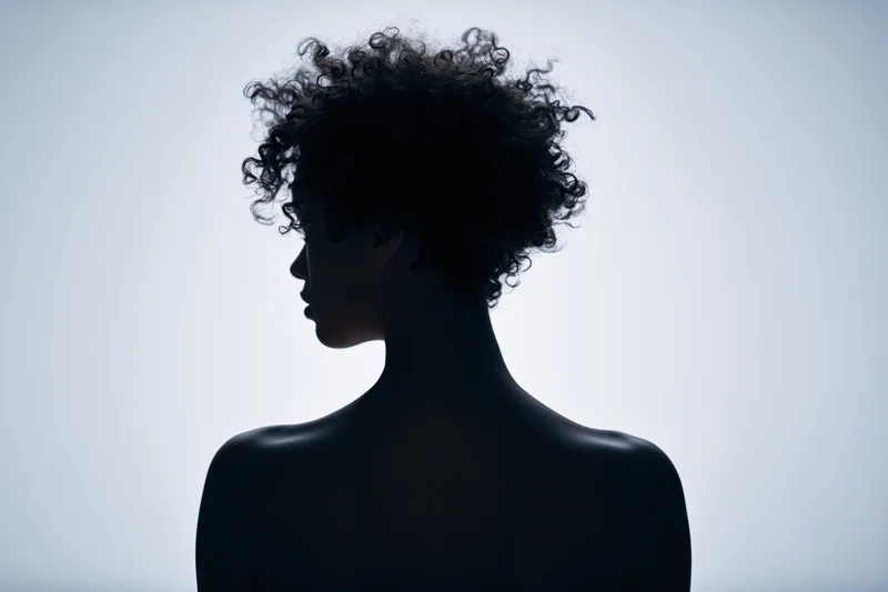 Silhouette of a woman with short curly hair in profile against a light background