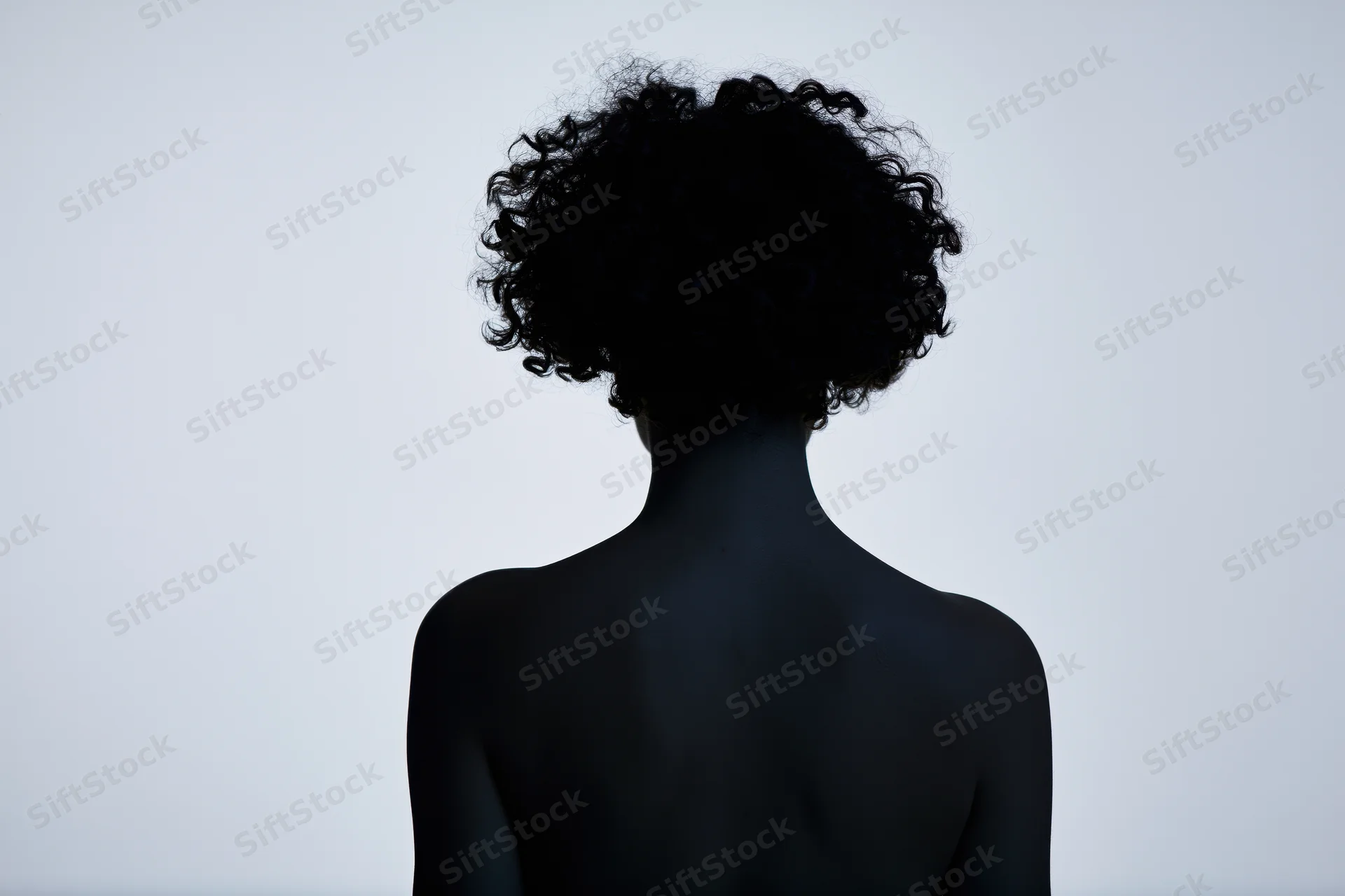 Silhouette of a woman with short curly hair standing still, back view against white background