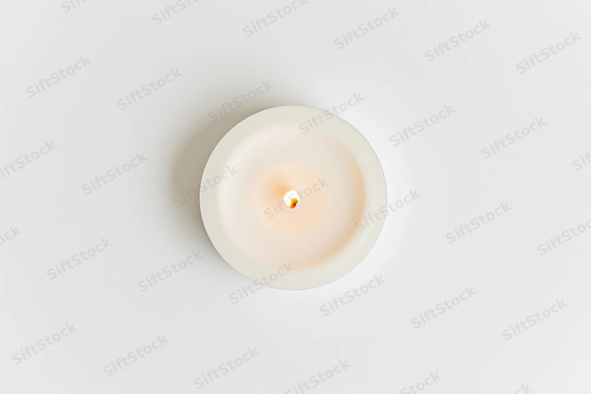 Overhead view of a lit white tealight candle on a plain white surface