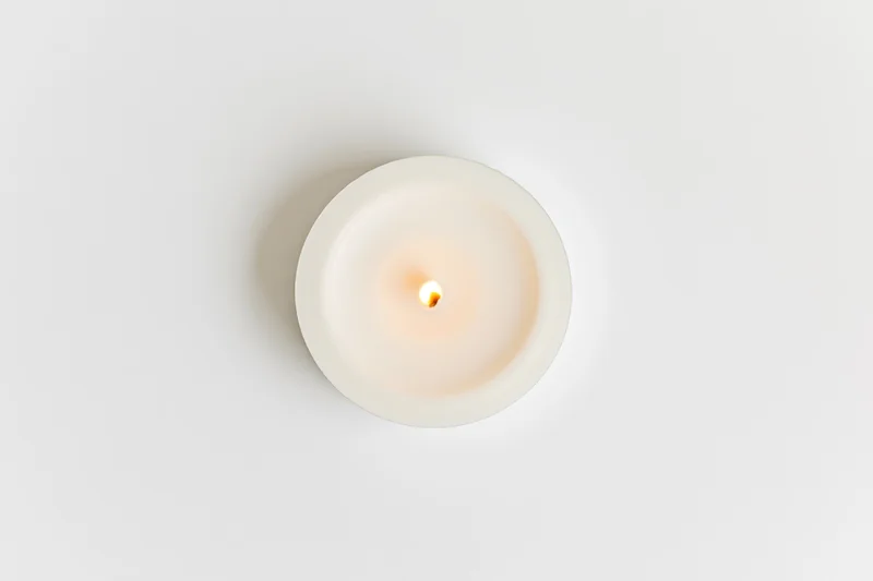 Overhead view of a lit white tealight candle on a plain white surface