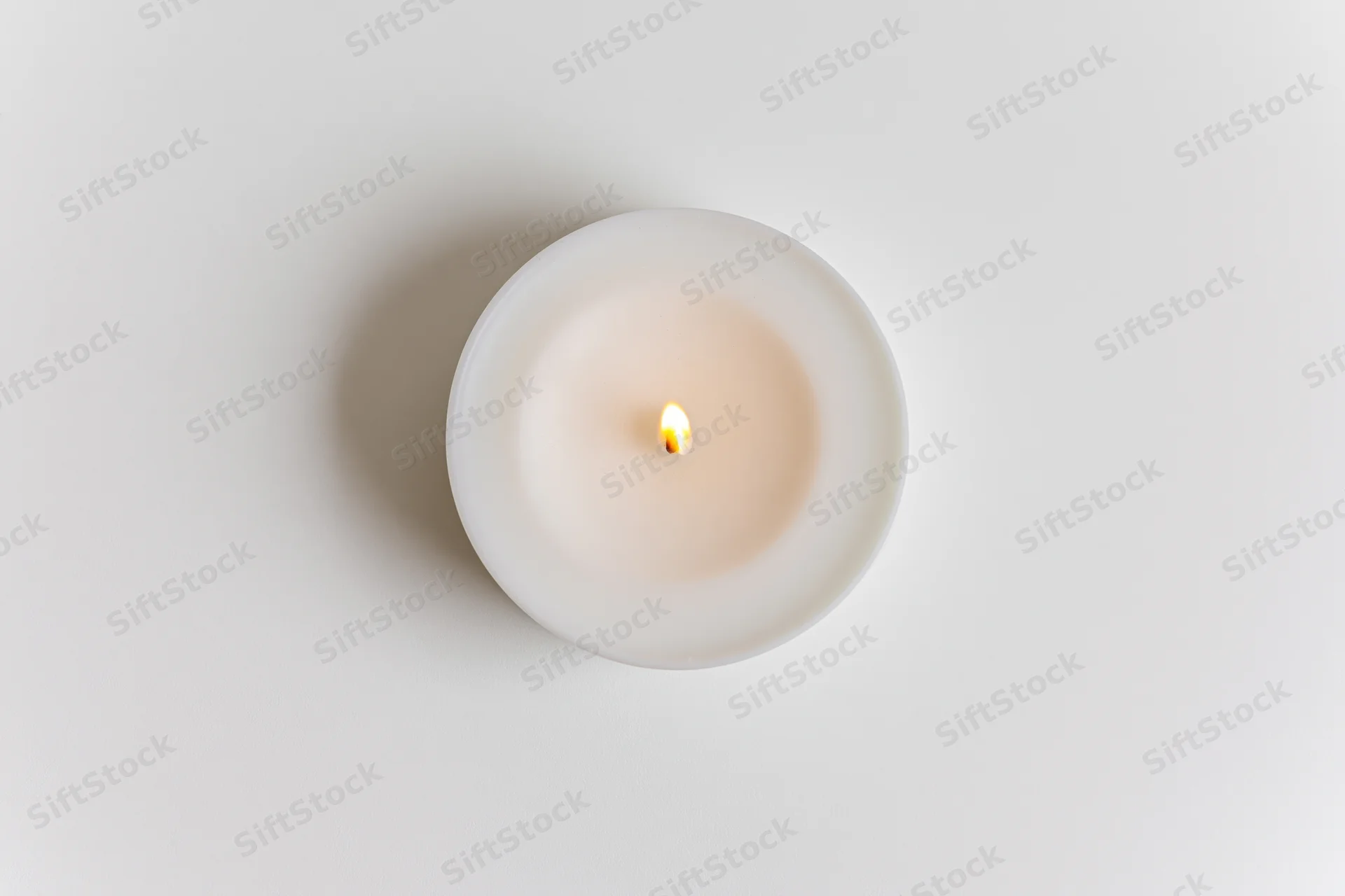 Lit tealight candle viewed from directly above on a white surface