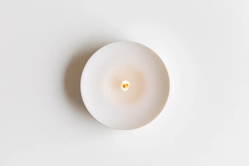 Overhead view of a lit white tealight candle on a plain white surface