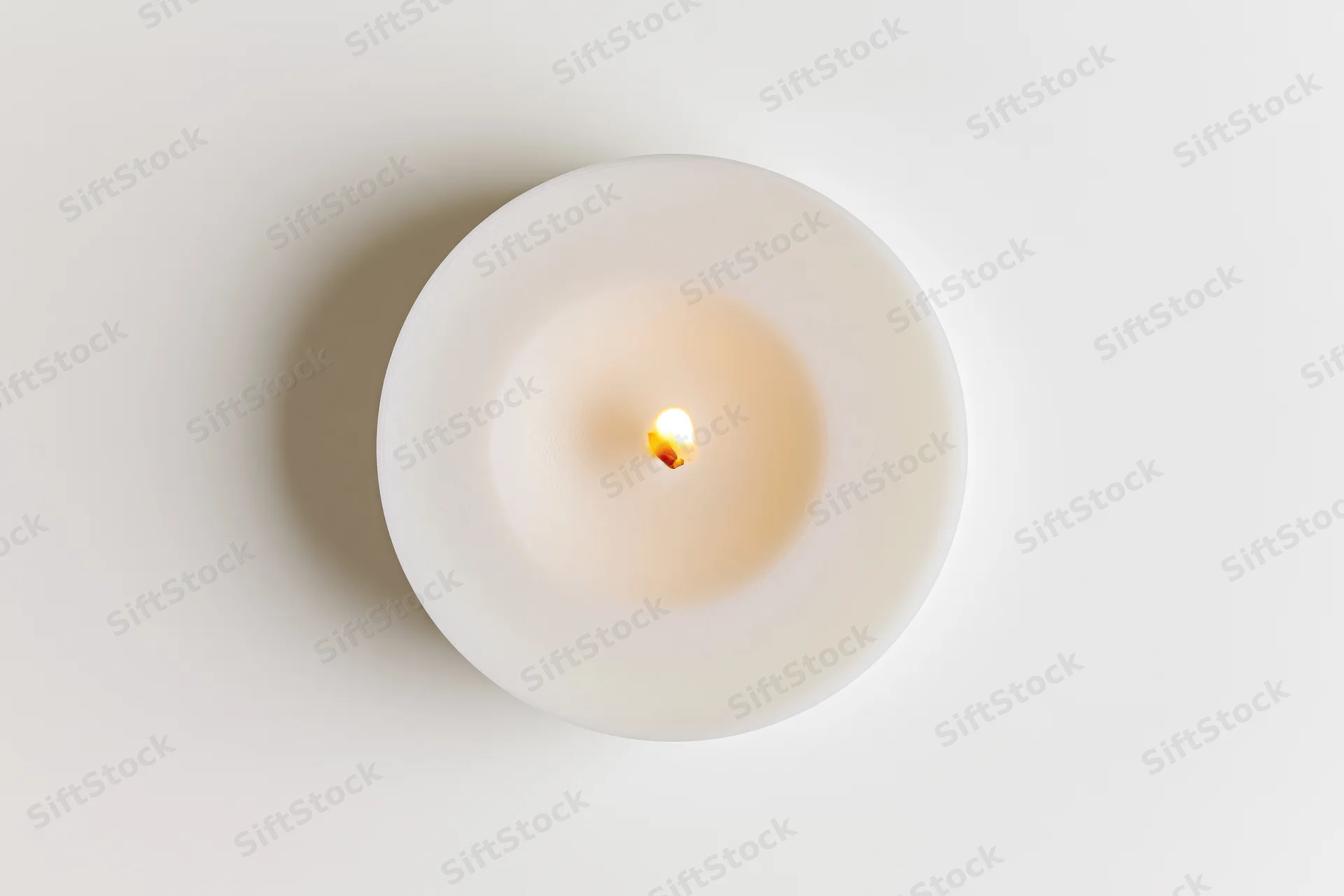 Overhead view of a lit white tealight candle on a plain surface