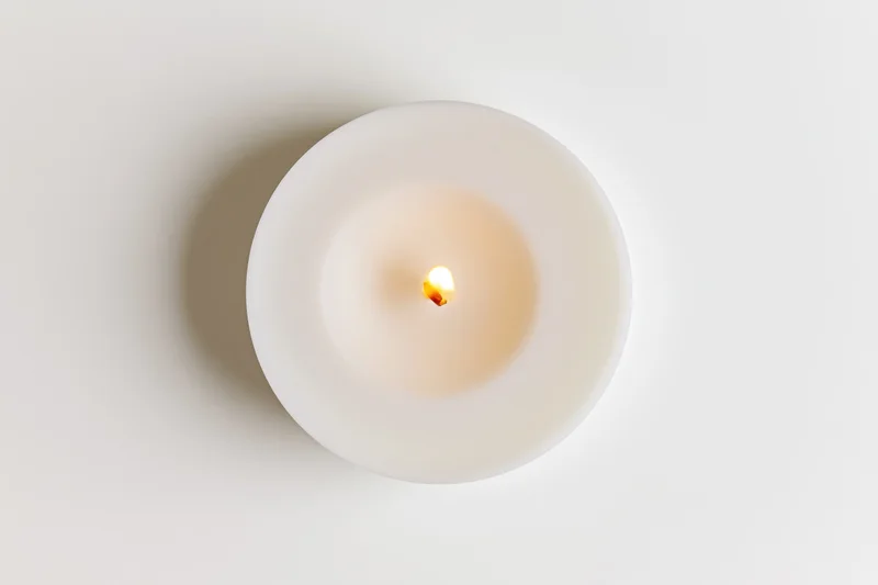 Overhead view of a lit white tealight candle on a plain surface