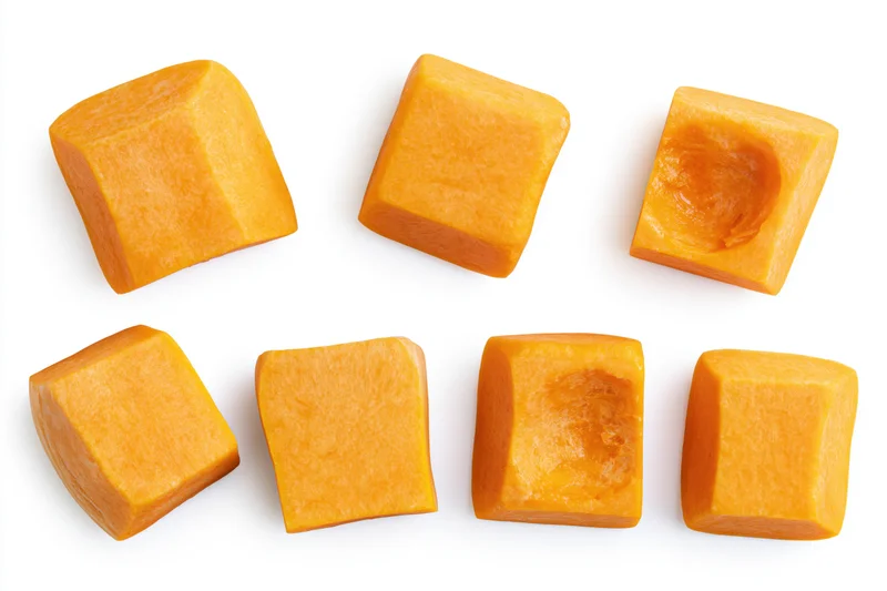 Raw butternut squash chunks arranged in two rows on white background
