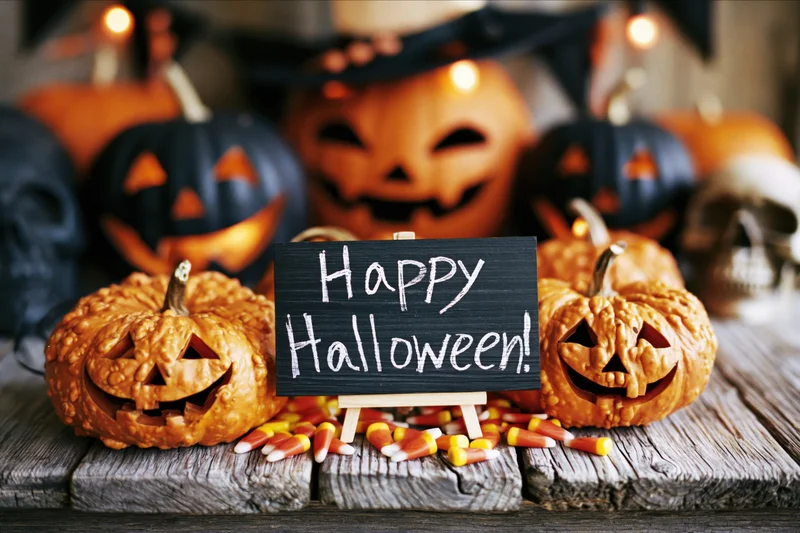 Carved pumpkins and candy corn arranged around a chalkboard sign reading happy halloween on a wooden table