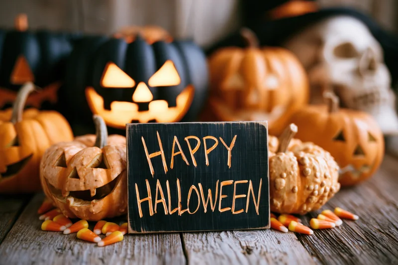 Carved pumpkins and candy corn arranged around a blackboard sign reading happy halloween on a wooden table