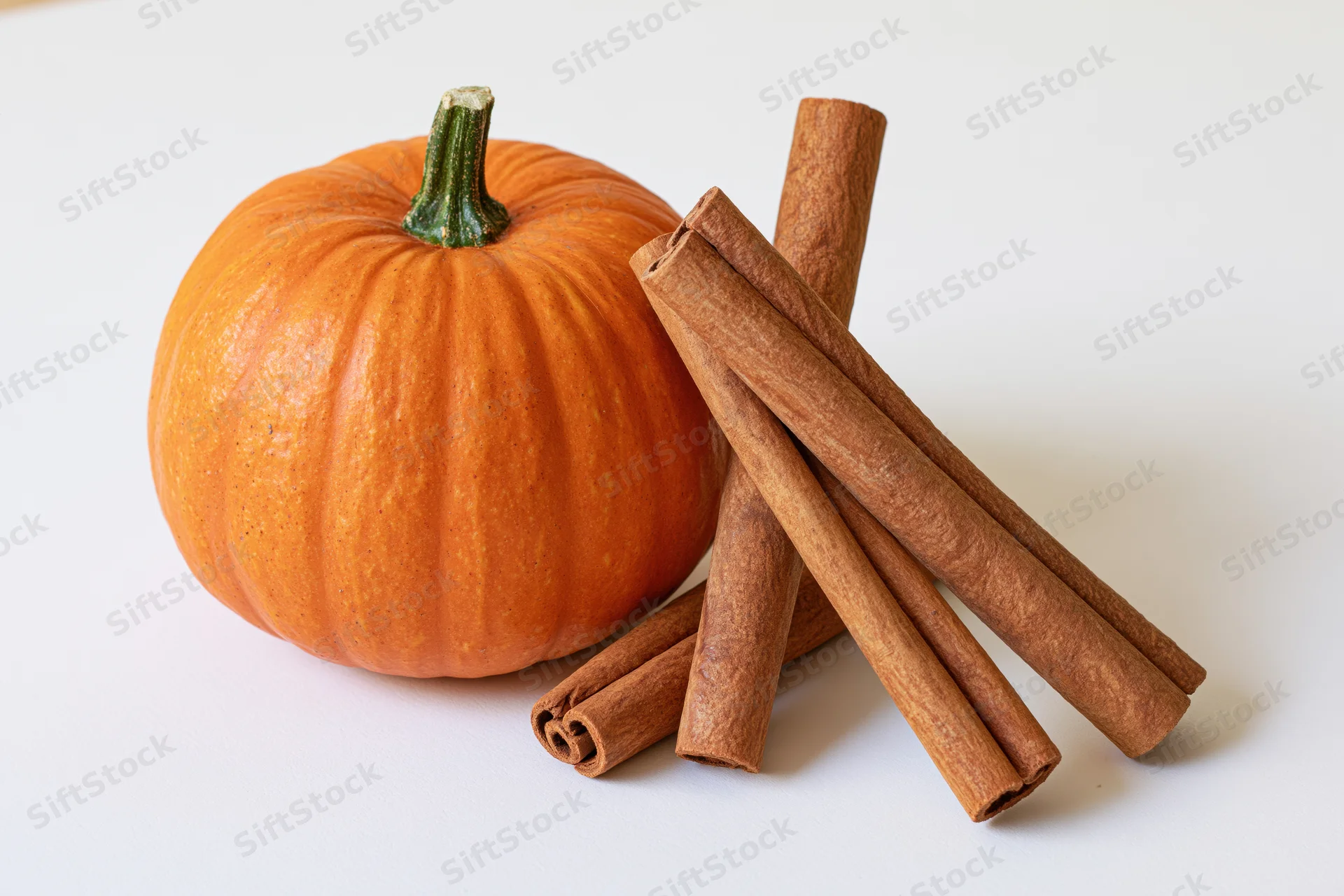 Small orange pumpkin beside a bundle of cinnamon sticks on a white surface