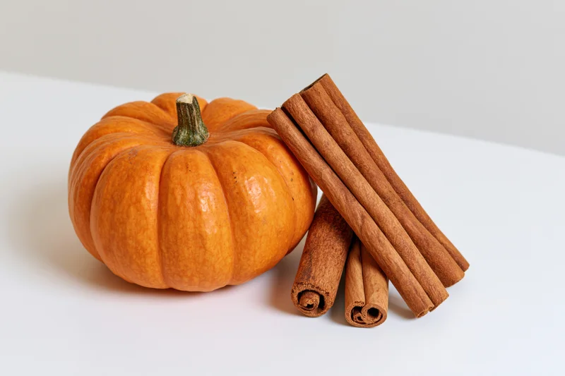 Small orange pumpkin beside cinnamon sticks on white surface