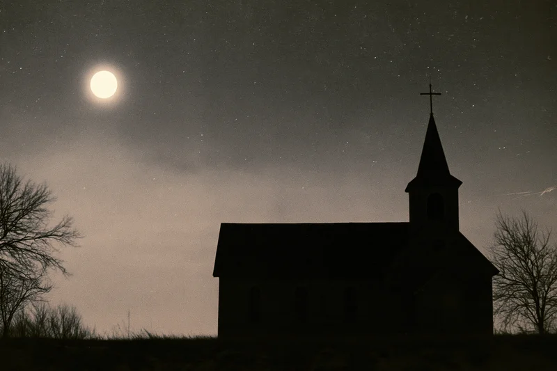 Silhouette of a small rural wooden church with a pointed steeple and cross under a full moon and starry night sky