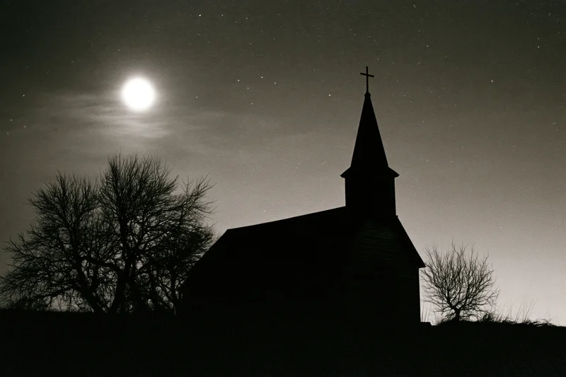 Silhouette of a small rural wooden church with a pointed steeple and cross under a full moon and starry night sky