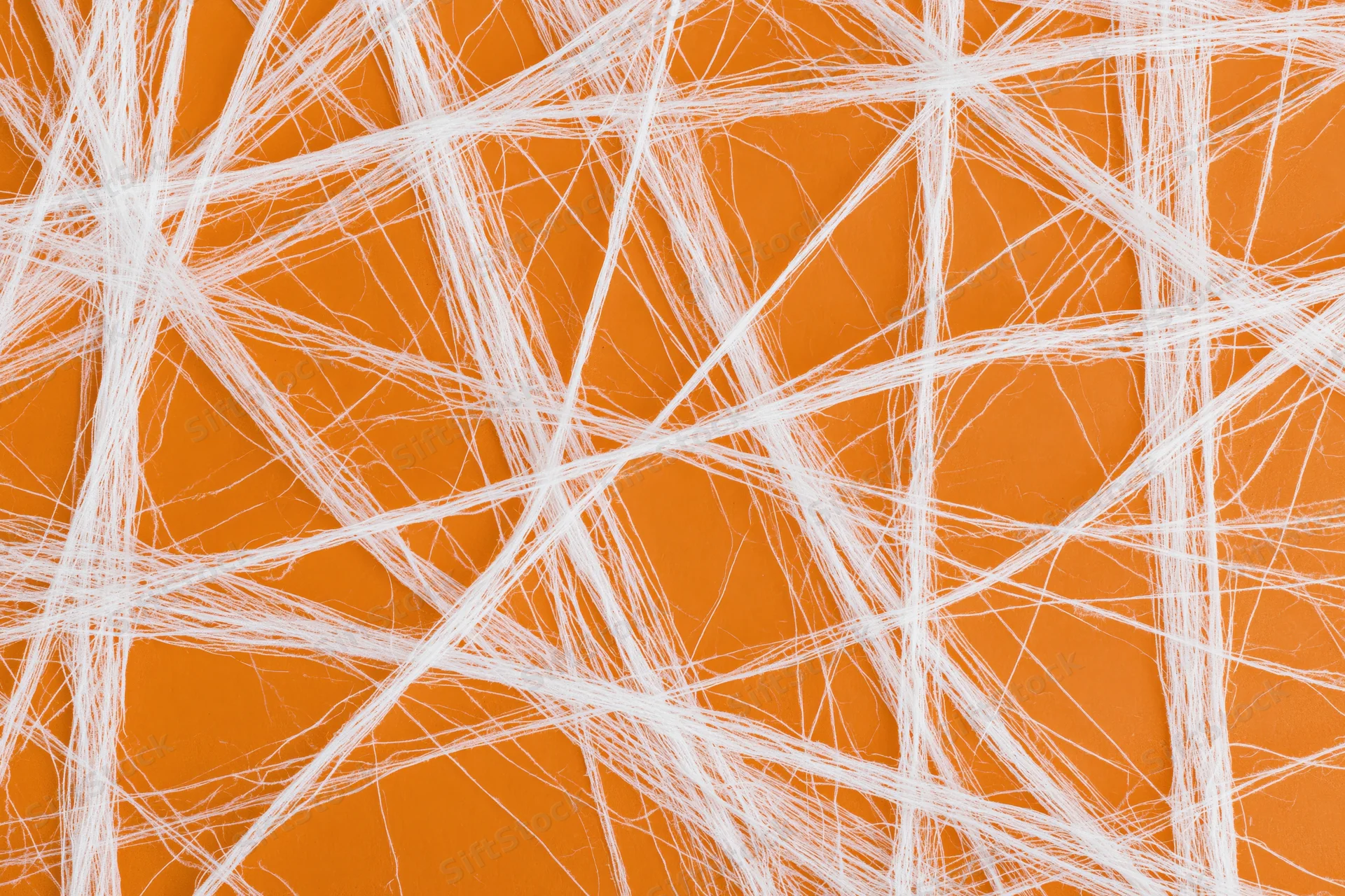 White artificial cobweb spread across orange surface in crisscross pattern