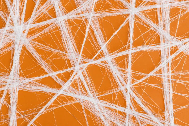 White artificial cobweb spread across orange surface in crisscross pattern