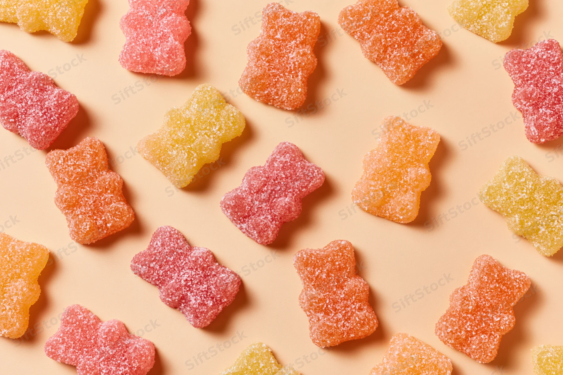 Sugar-coated gummy bear candies in pink orange and yellow scattered on a pastel peach background in a flat lay top view