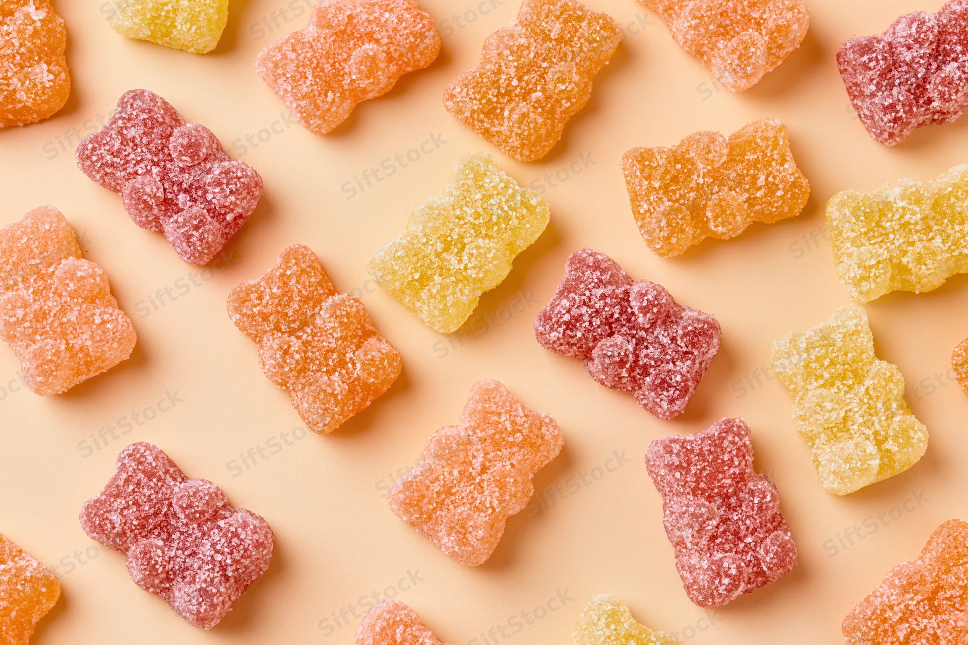 Sugar-coated gummy bear candies in pink orange and yellow scattered on a pastel surface in a flat lay arrangement