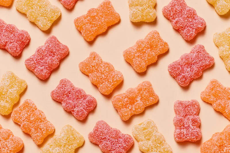 Sugar-coated gummy bear candies in pink, orange and yellow arranged in a flat lay on a pastel background