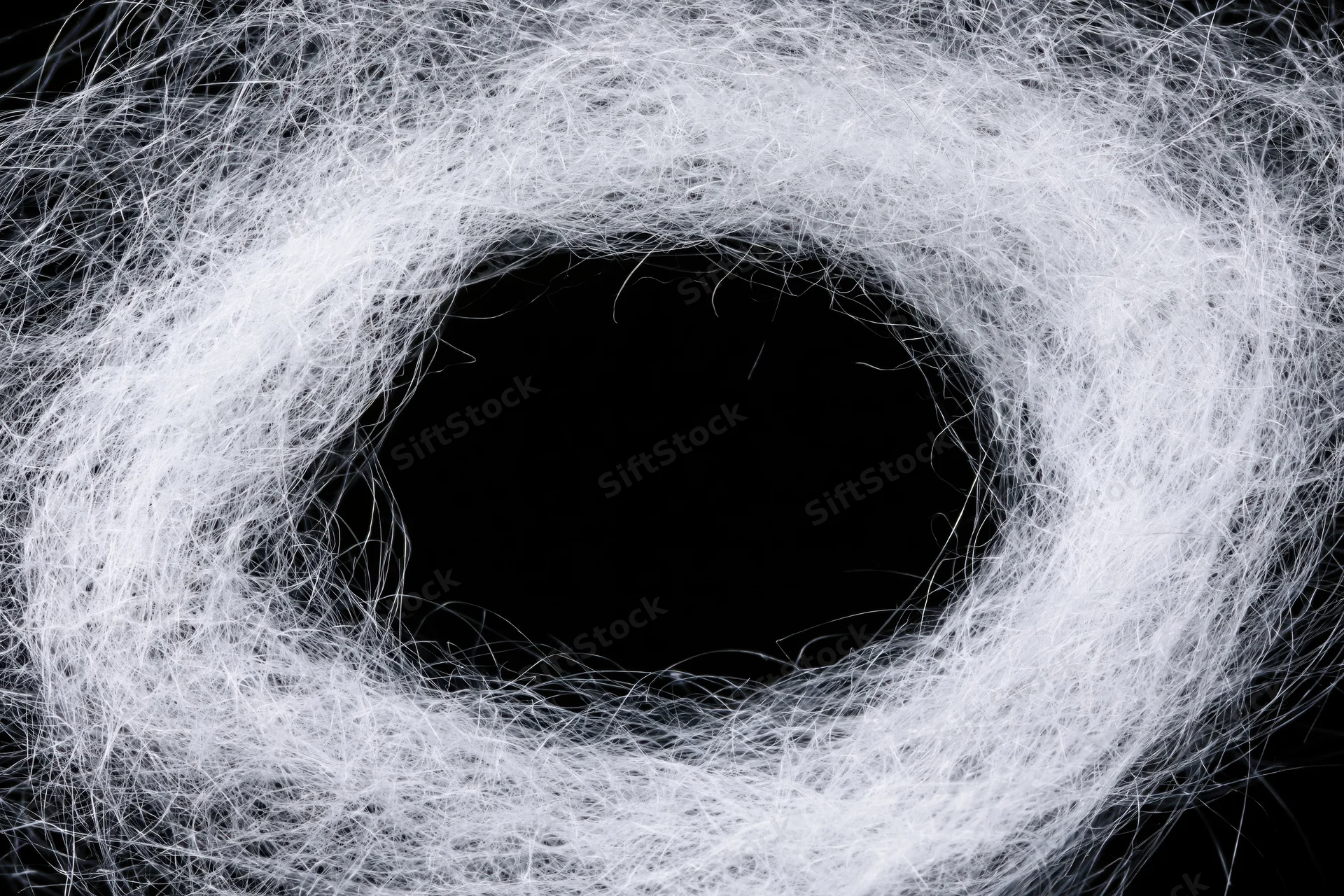 Tangled white synthetic spiderweb fibers forming a circular hole against black background