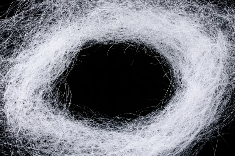 Tangled white synthetic spiderweb fibers forming a circular hole against black background