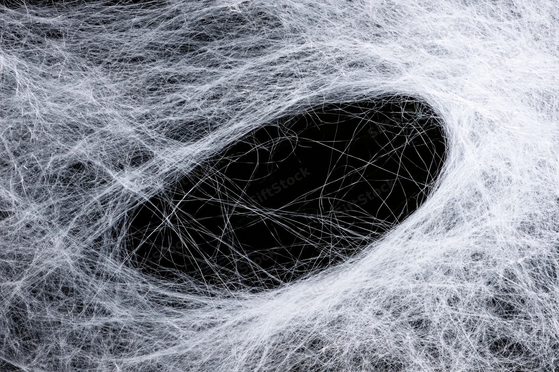 Tangled white synthetic spiderweb material forming a dense web against black background