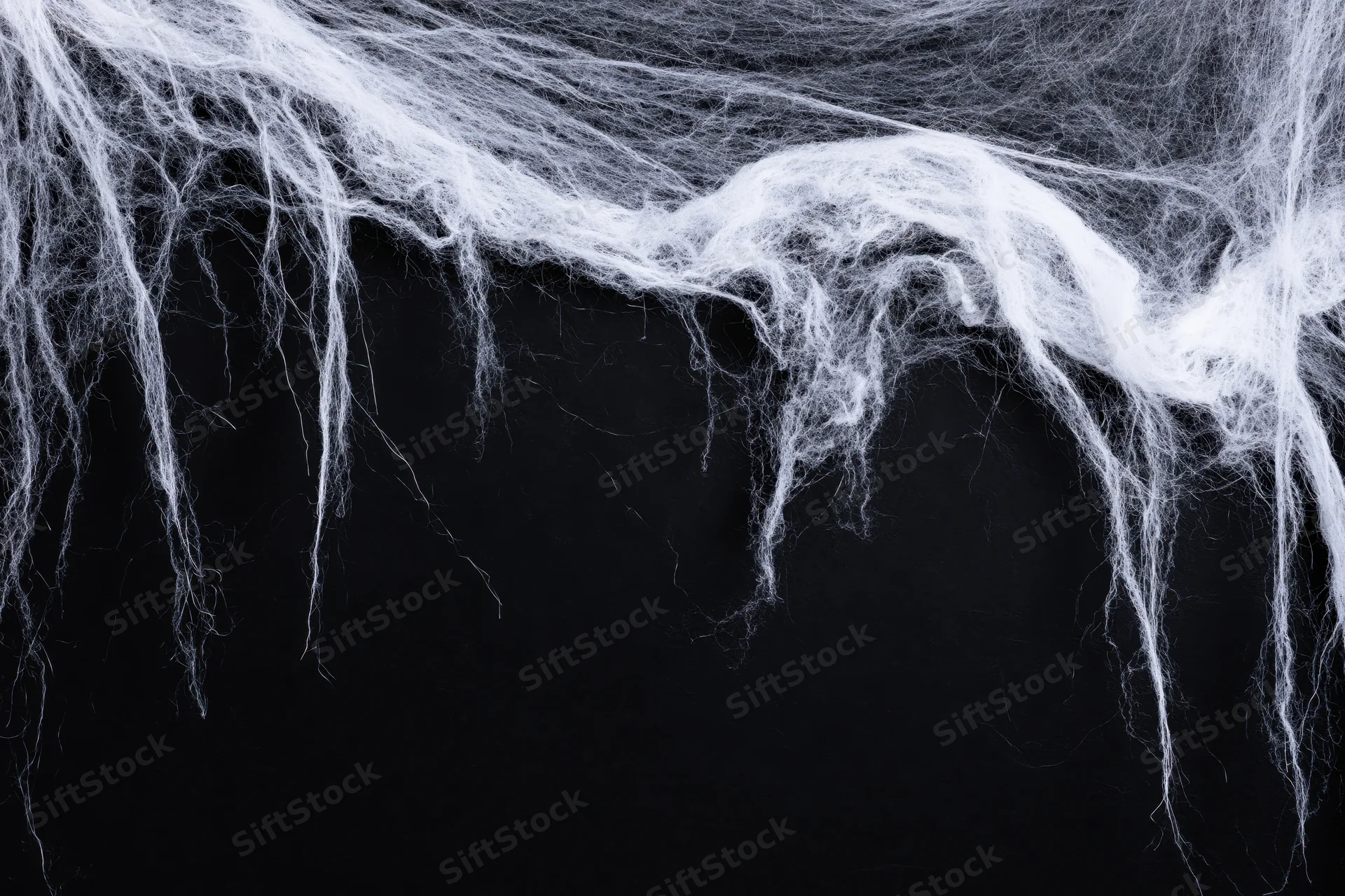 Tangled white artificial spiderweb draped across black background with copyspace below