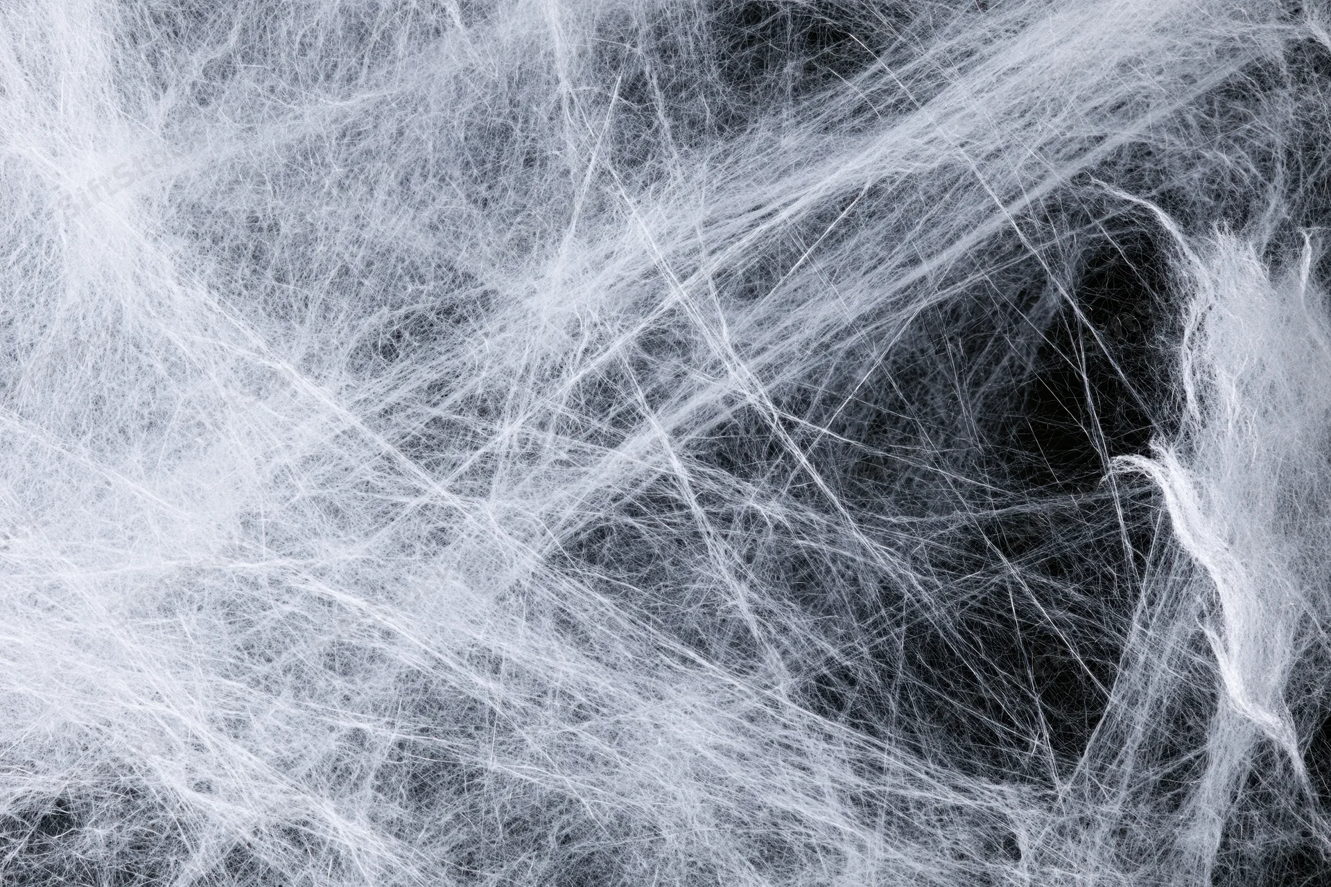 Tangled white synthetic fibers forming a web-like texture against dark background