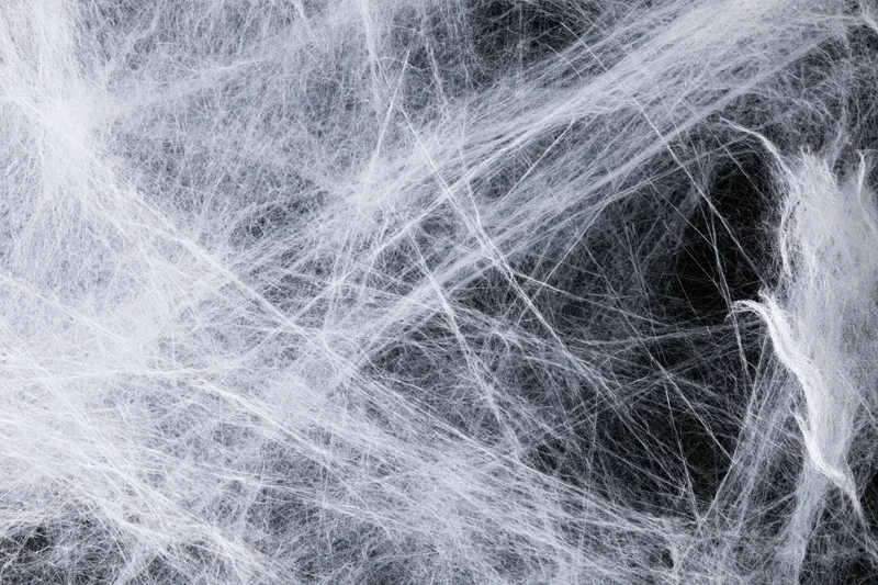 Tangled white synthetic fibers forming a web-like texture against dark background