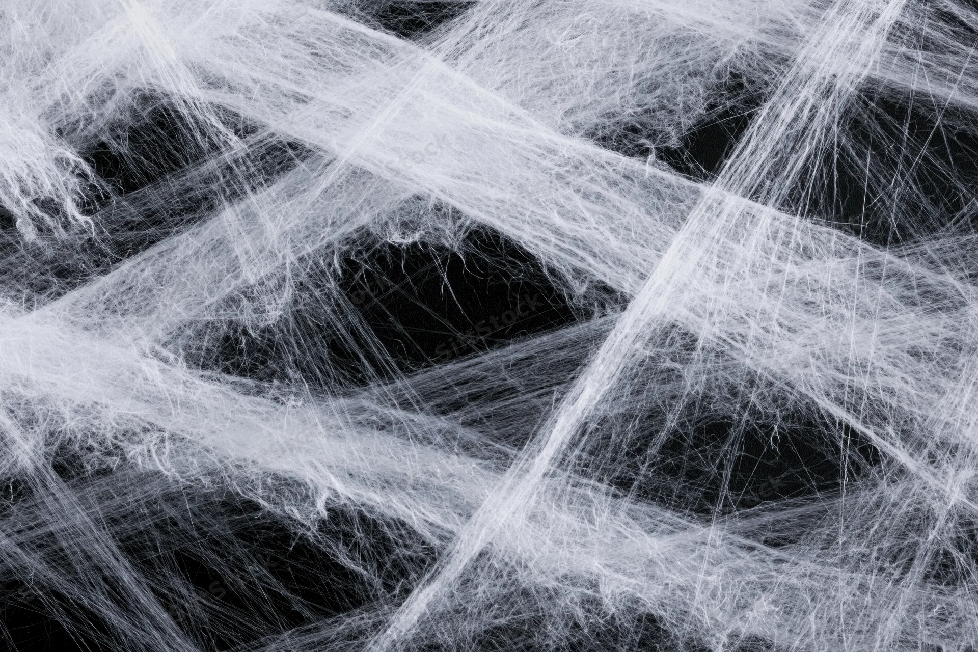 Tangled white synthetic spiderweb material stretched across a dark background