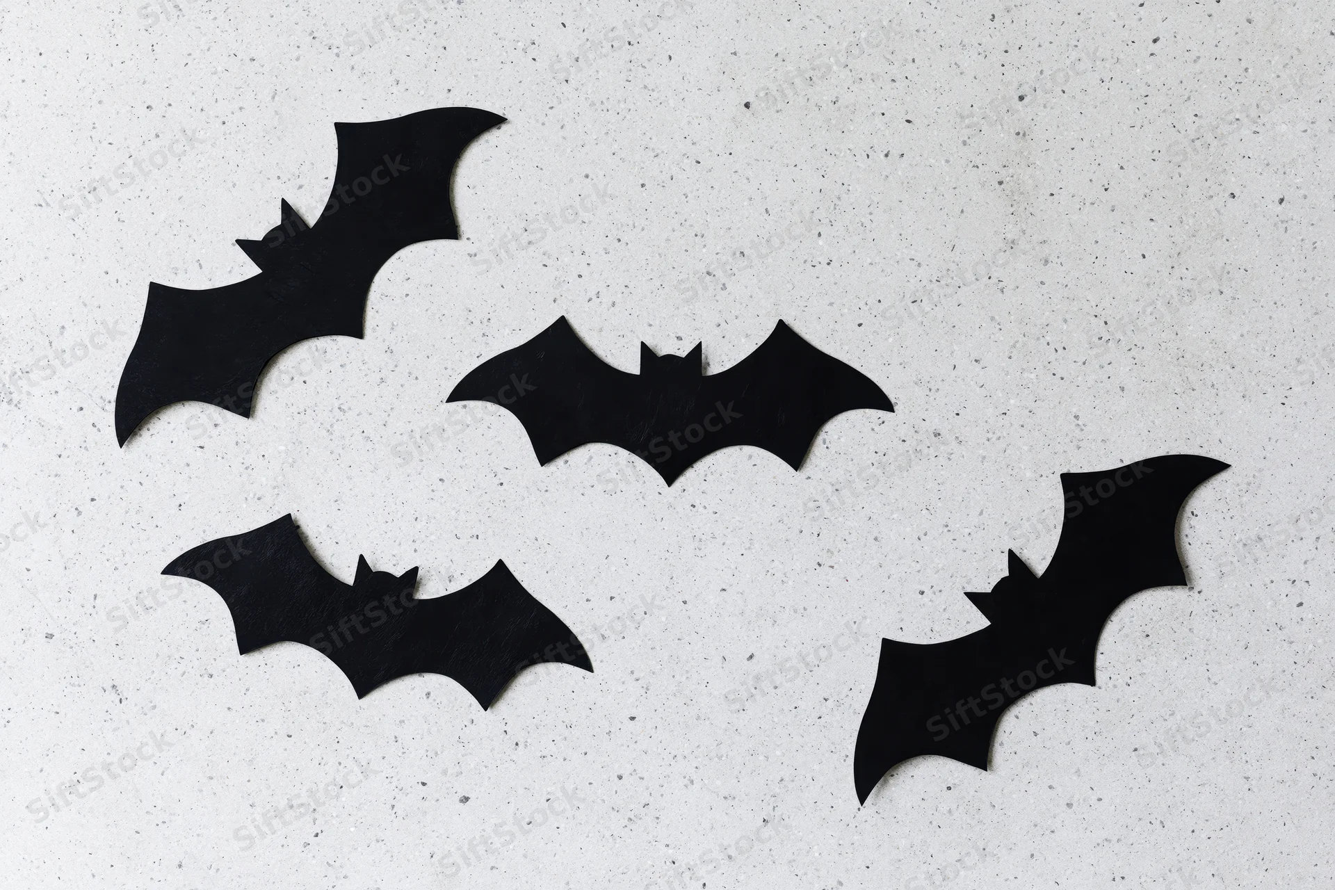 Black paper bat cutouts arranged on a speckled white surface for halloween decoration