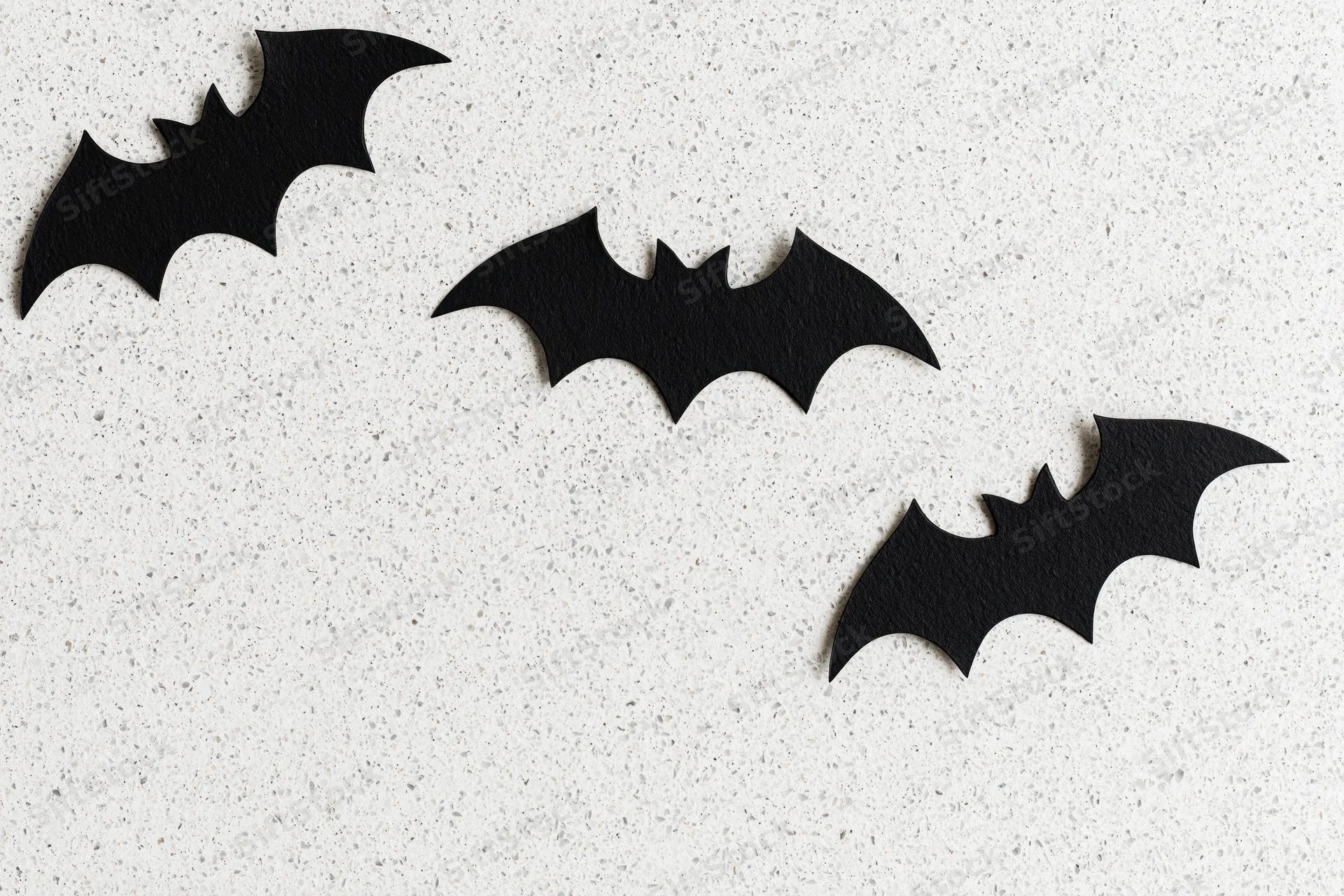 Three black paper bat cutouts arranged on a speckled white surface for halloween decoration