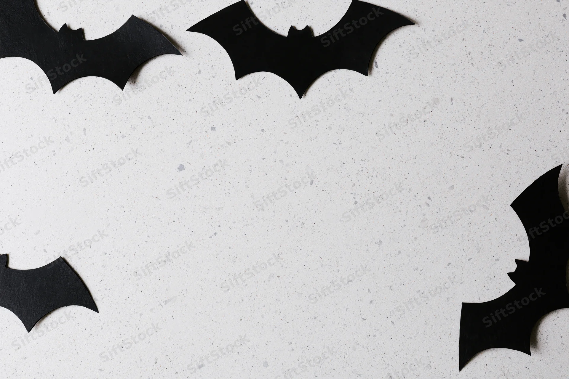 Black paper bat cutouts arranged as halloween decoration on white speckled surface
