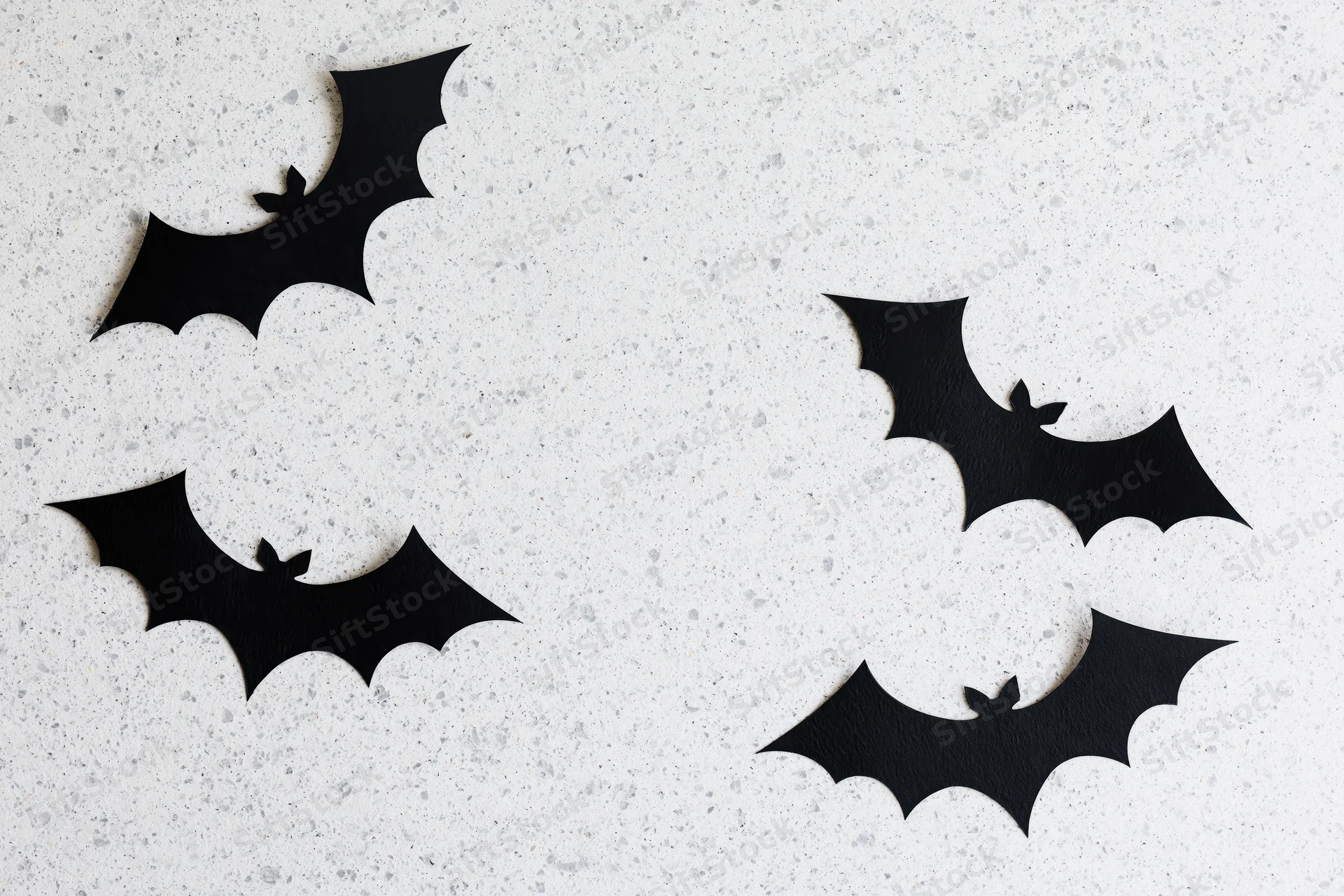 Black paper bat cutouts arranged as halloween decoration on speckled white surface
