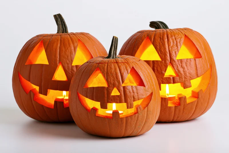Three carved pumpkins glowing with candles arranged together on a white surface