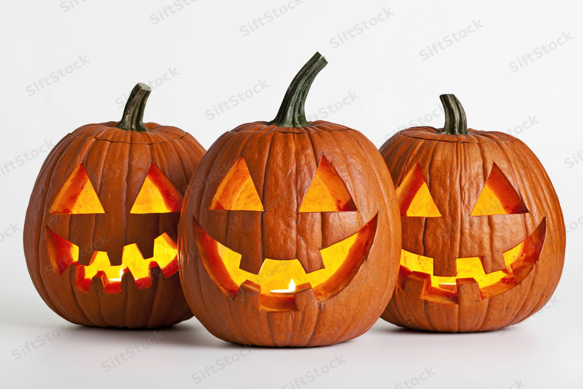 Three carved pumpkins glowing with candles inside, arranged in a row on a white surface