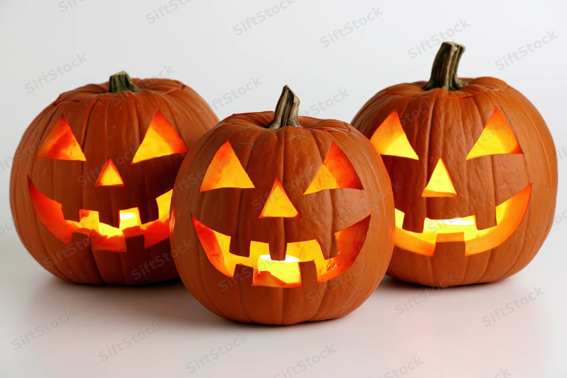 Three carved pumpkins glowing with light arranged in a row on a white surface