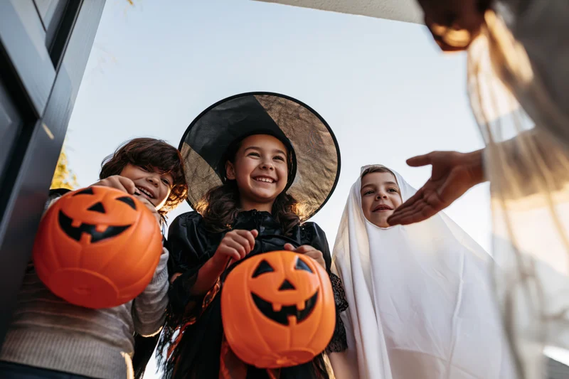Three children in halloween costumes smiling while trick-or-treating at a front door