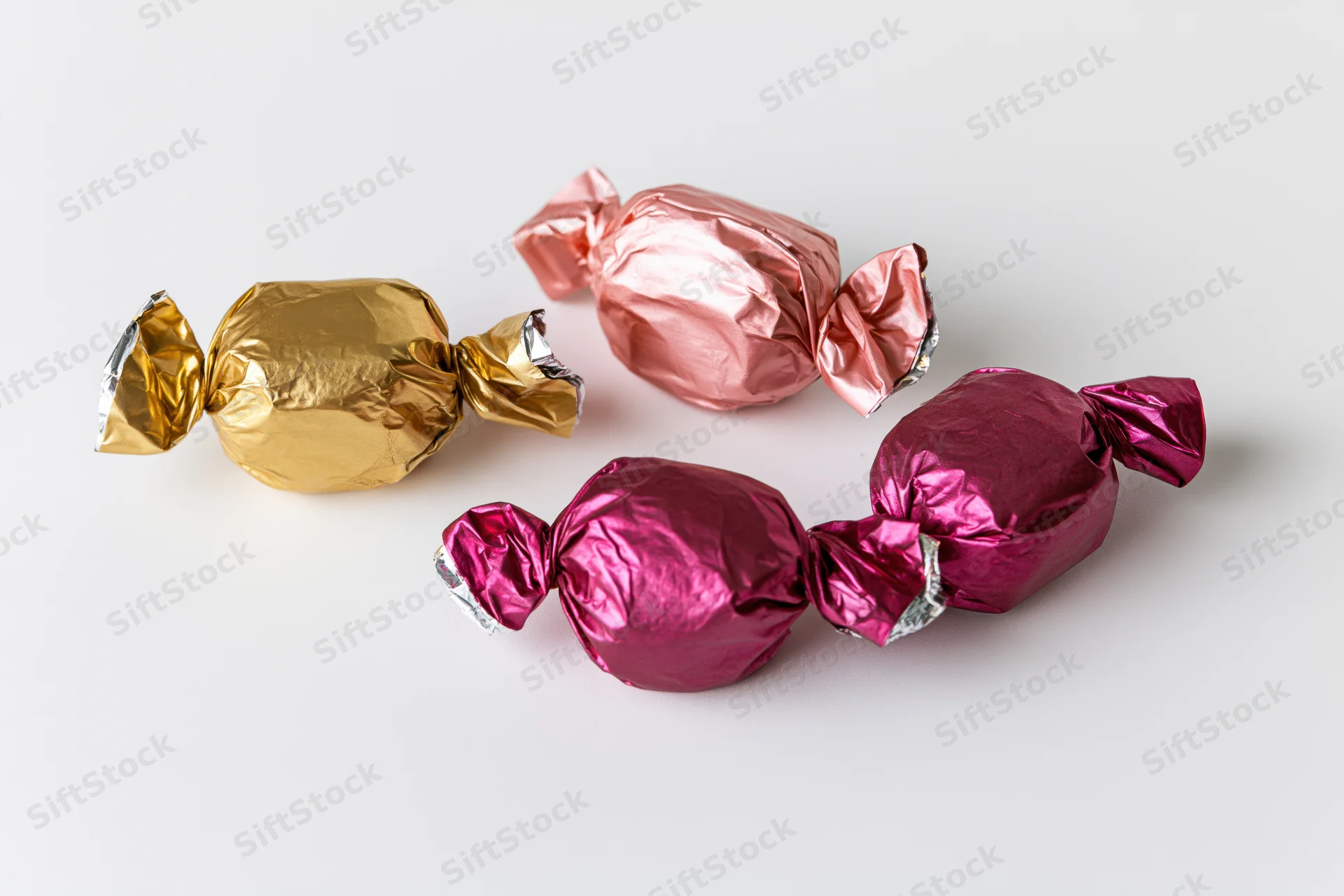 Foil-wrapped candies in gold, pink and magenta arranged loosely on a white surface