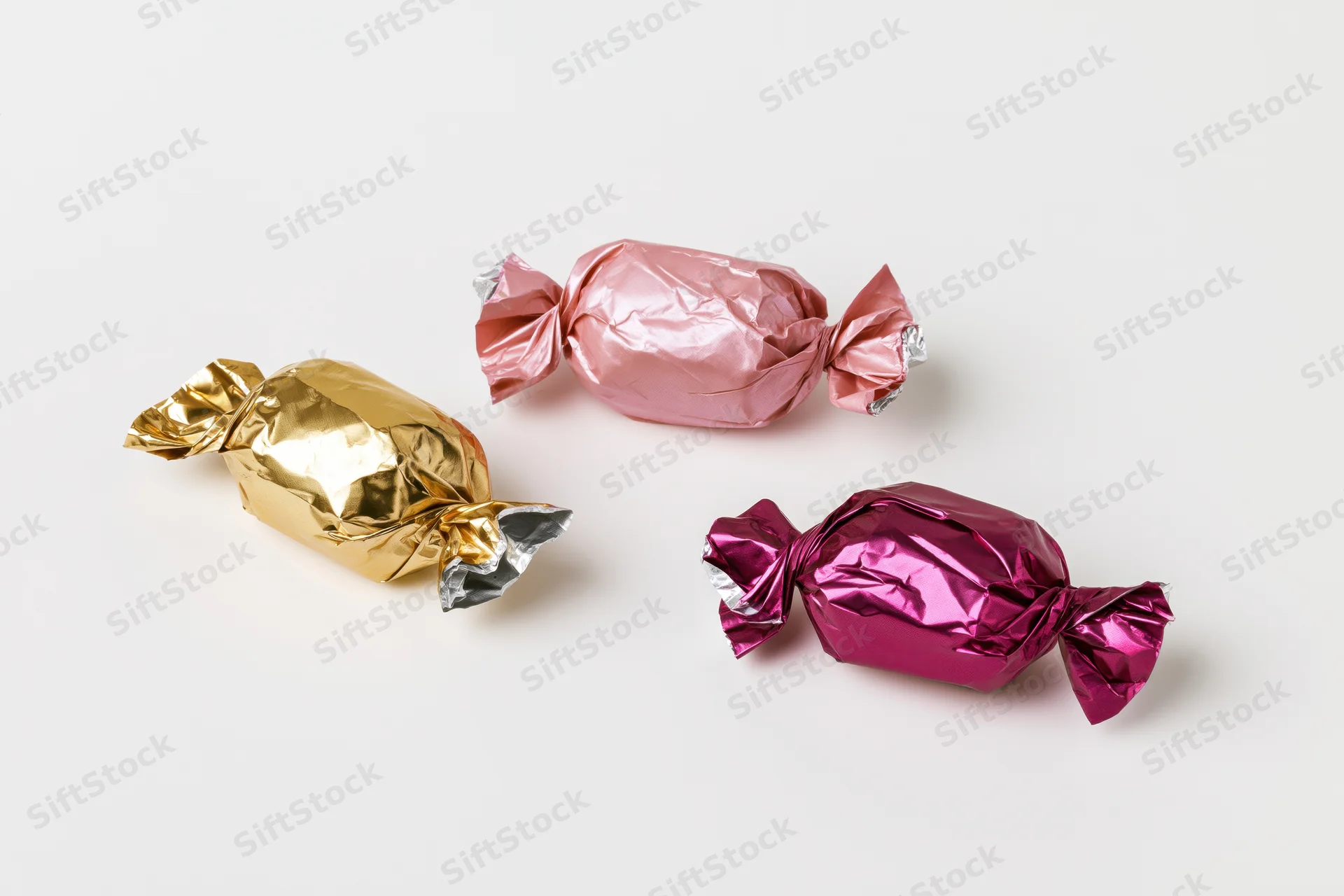 Three foil-wrapped candies in gold, pink and purple arranged on a white surface