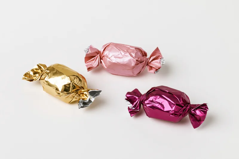 Three foil-wrapped candies in gold, pink and purple arranged on a white surface