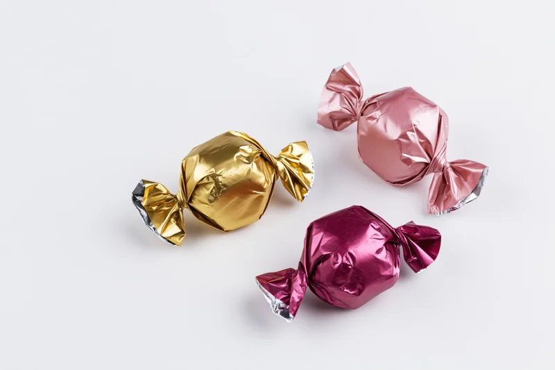 Three foil-wrapped candies in gold, pink and magenta arranged on a white surface