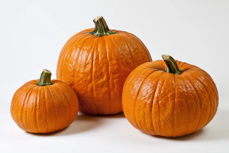 Three orange pumpkins of varying sizes arranged together on a white surface