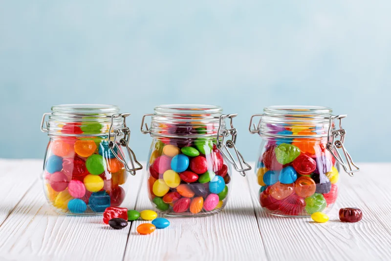 Three glass jars filled with colorful candies arranged on a white wooden table