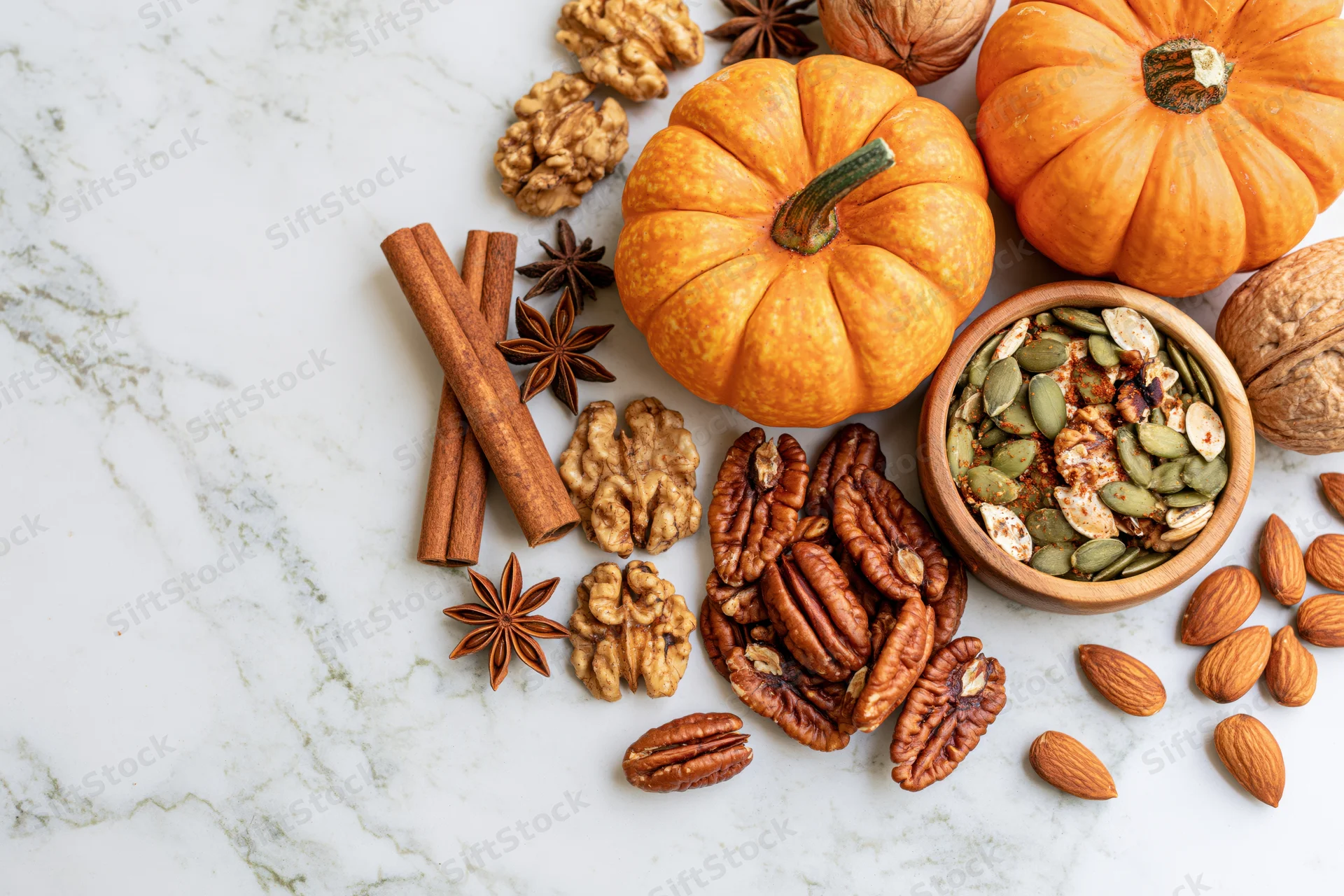 Small pumpkins and autumn spices arranged with nuts on a marble surface