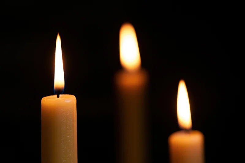 Three lit candles in focus against a dark background with soft glow and shallow depth of field